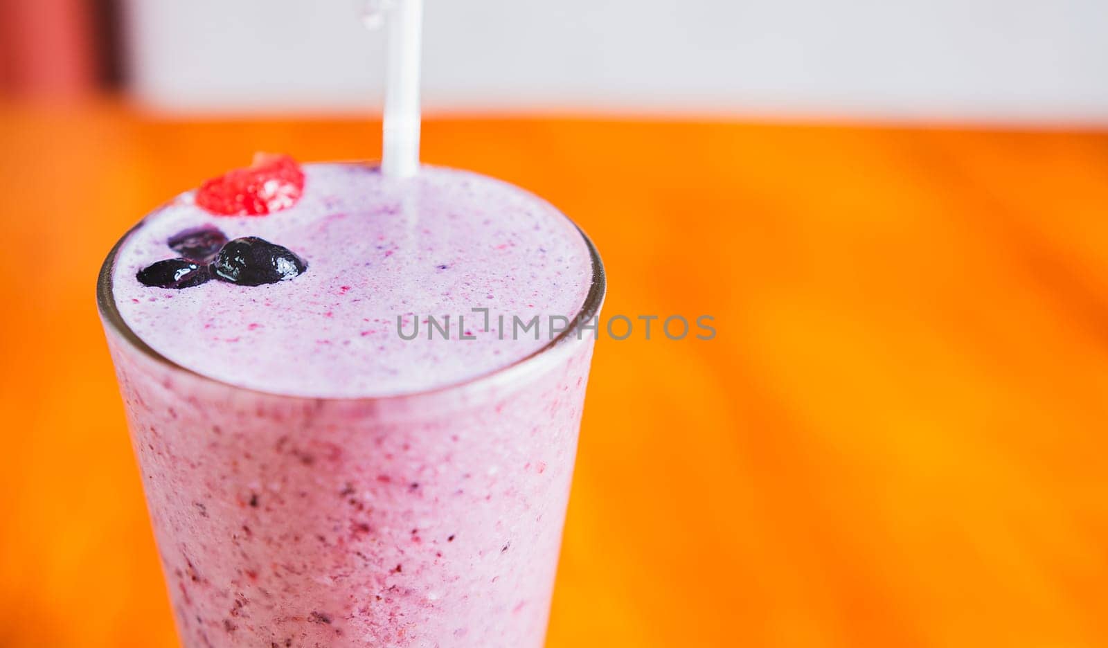 Close up of a strawberry milkshake in blurred background with copy space. Strawberry smoothie with blueberry on wooden background by isaiphoto