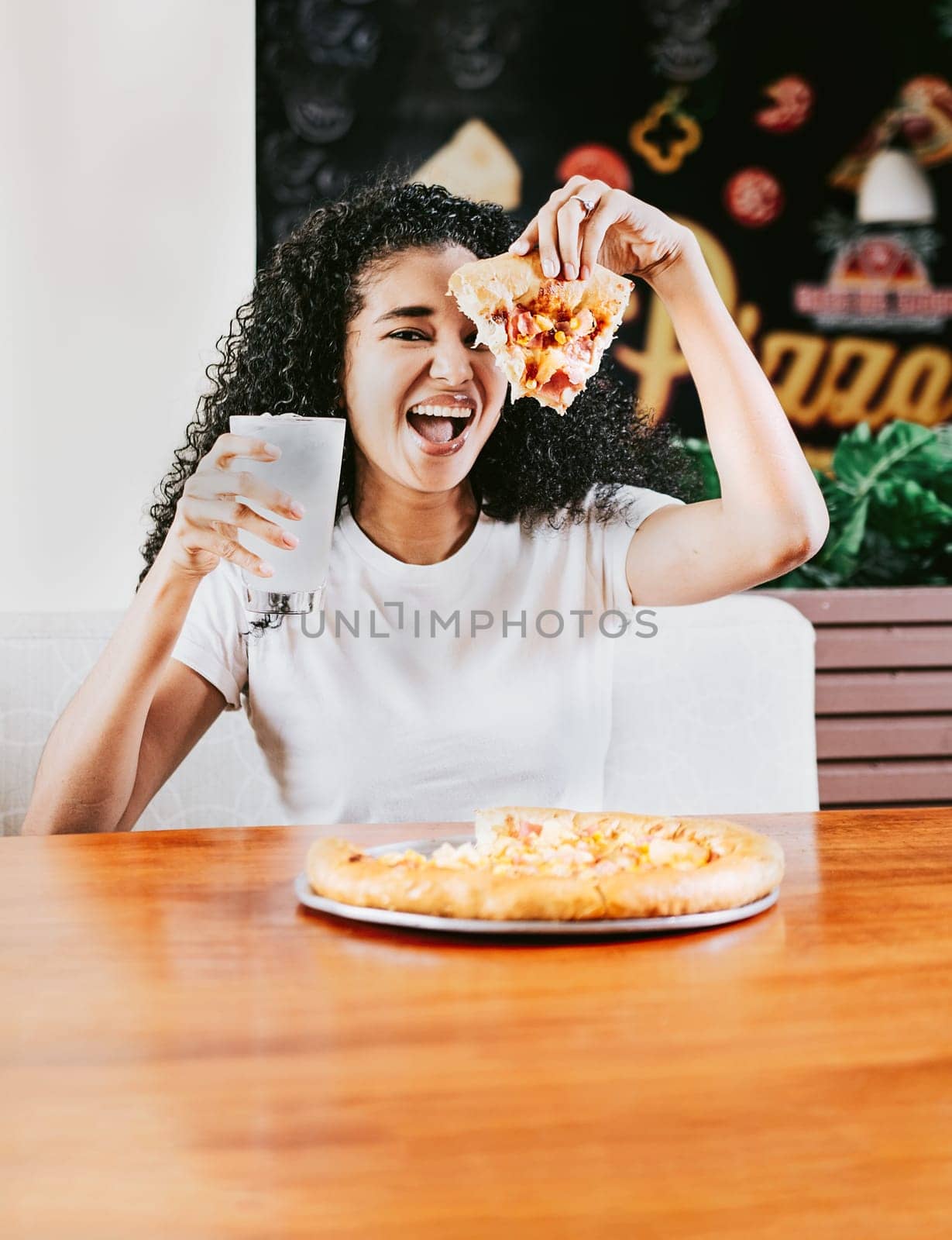 Happy afro hair woman showing slice of pizza in a restaurant. Smiling afro woman enjoying a pizza in a restaurant by isaiphoto