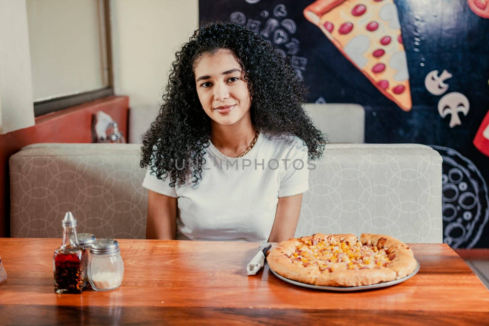 Portrait of a beautiful girl in a pizzeria. Young curly haired woman sitting in a pizzeria