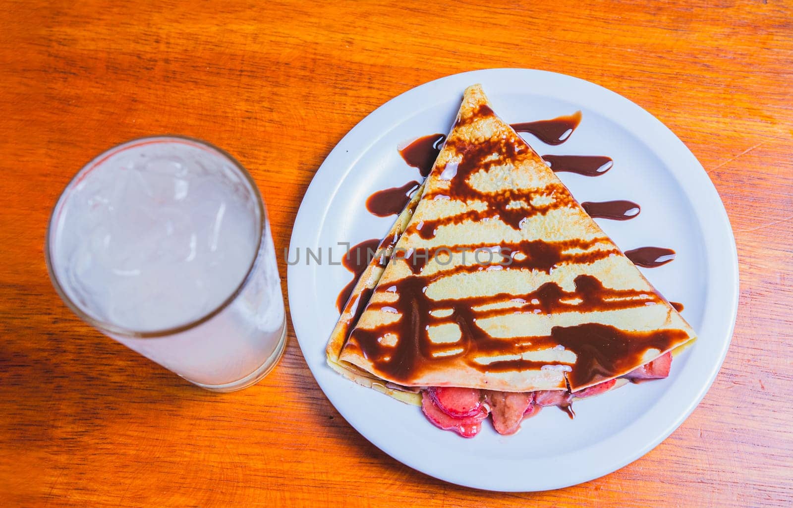 Crepe with chocolate cream and strawberry with drink on the table. Sweet strawberry crepe with chocolate cream and lemonade on table