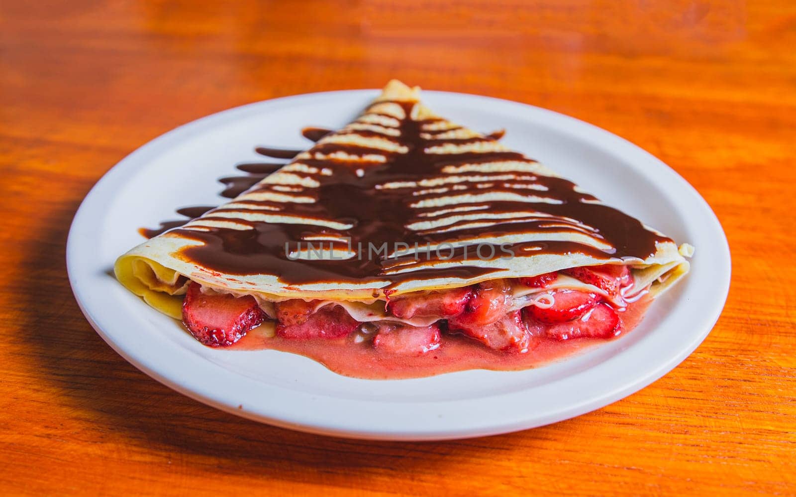 Close up of sweet strawberry crepe with chocolate cream on wooden table. Crepe with chocolate cream and strawberry on wooden table