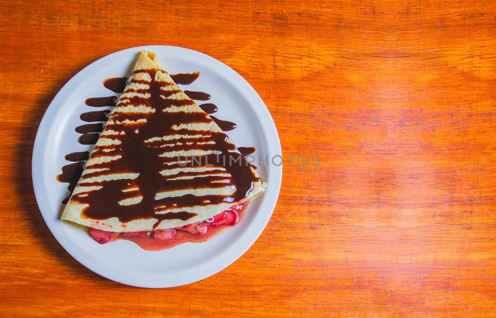 Crepe with chocolate cream and strawberry on wooden table. Sweet strawberry crepe with chocolate cream on wooden table
