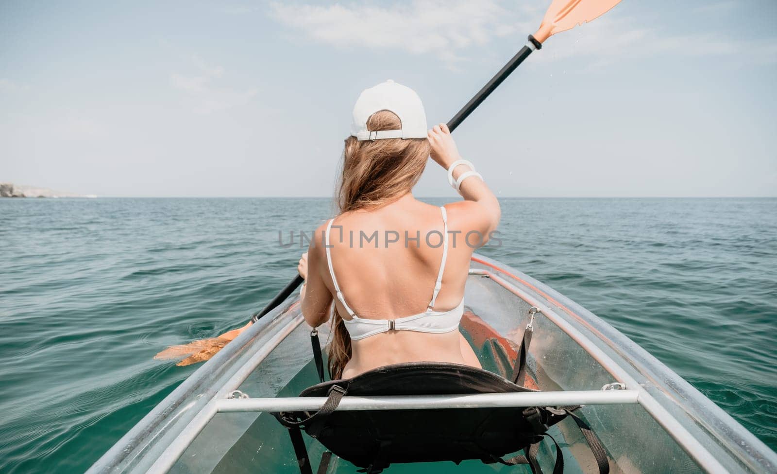 Woman in kayak back view. Happy young woman with long hair floating in transparent kayak on the crystal clear sea. Summer holiday vacation and cheerful female people relaxing having fun on the boat by panophotograph