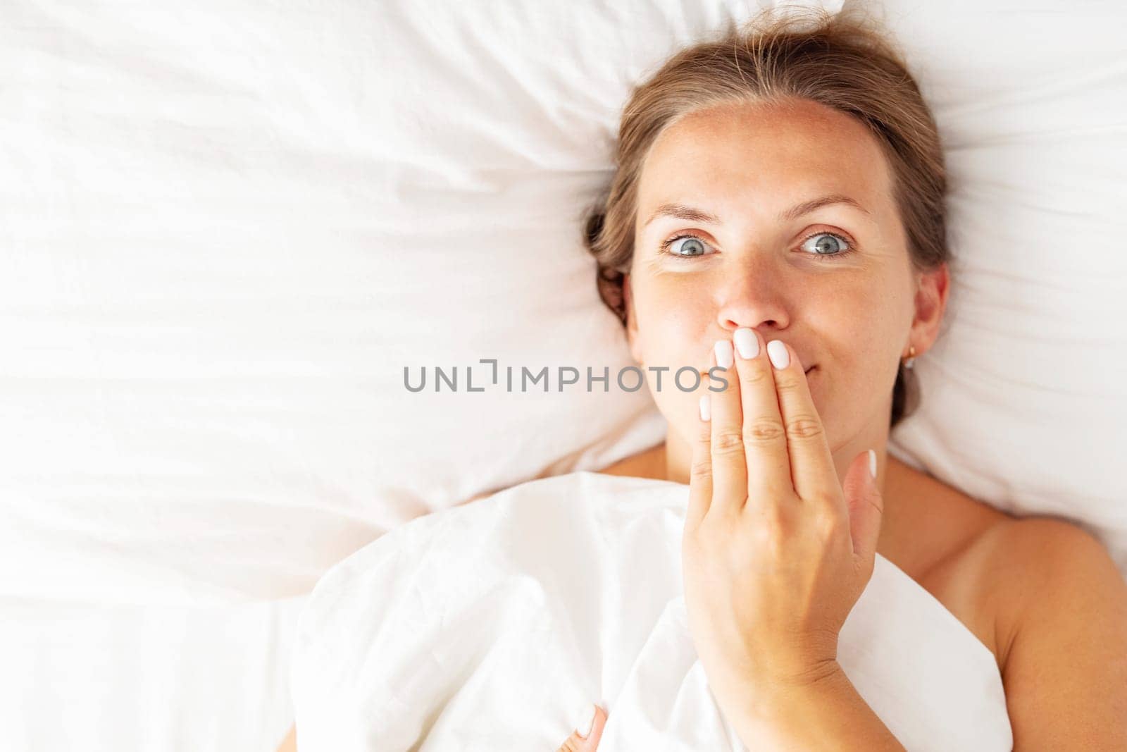 Young woman lies in bed and covers her mouth with her hand by andreyz