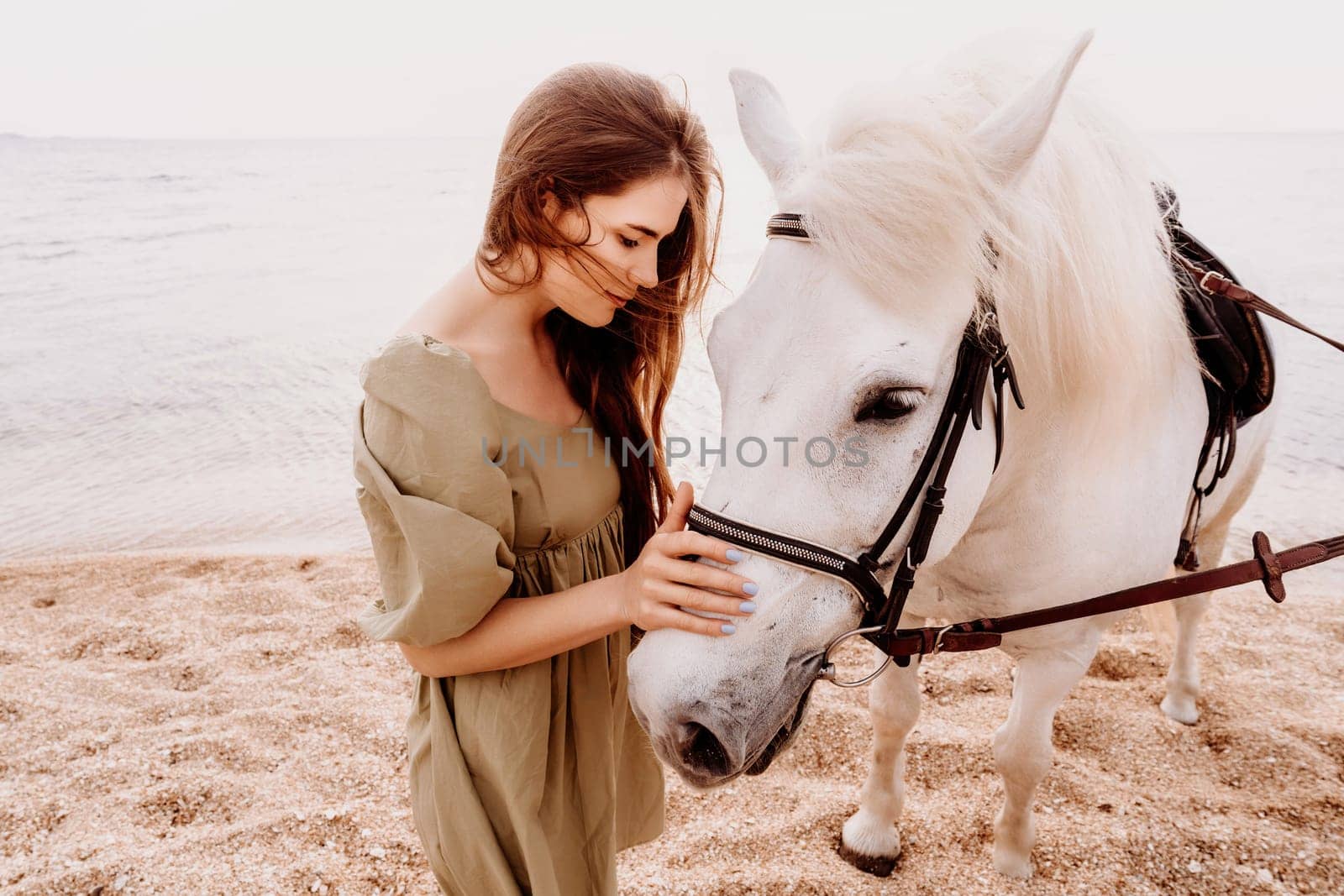 A white horse and a woman in a dress stand on a beach, with the sky and sea creating a picturesque backdrop for the scene