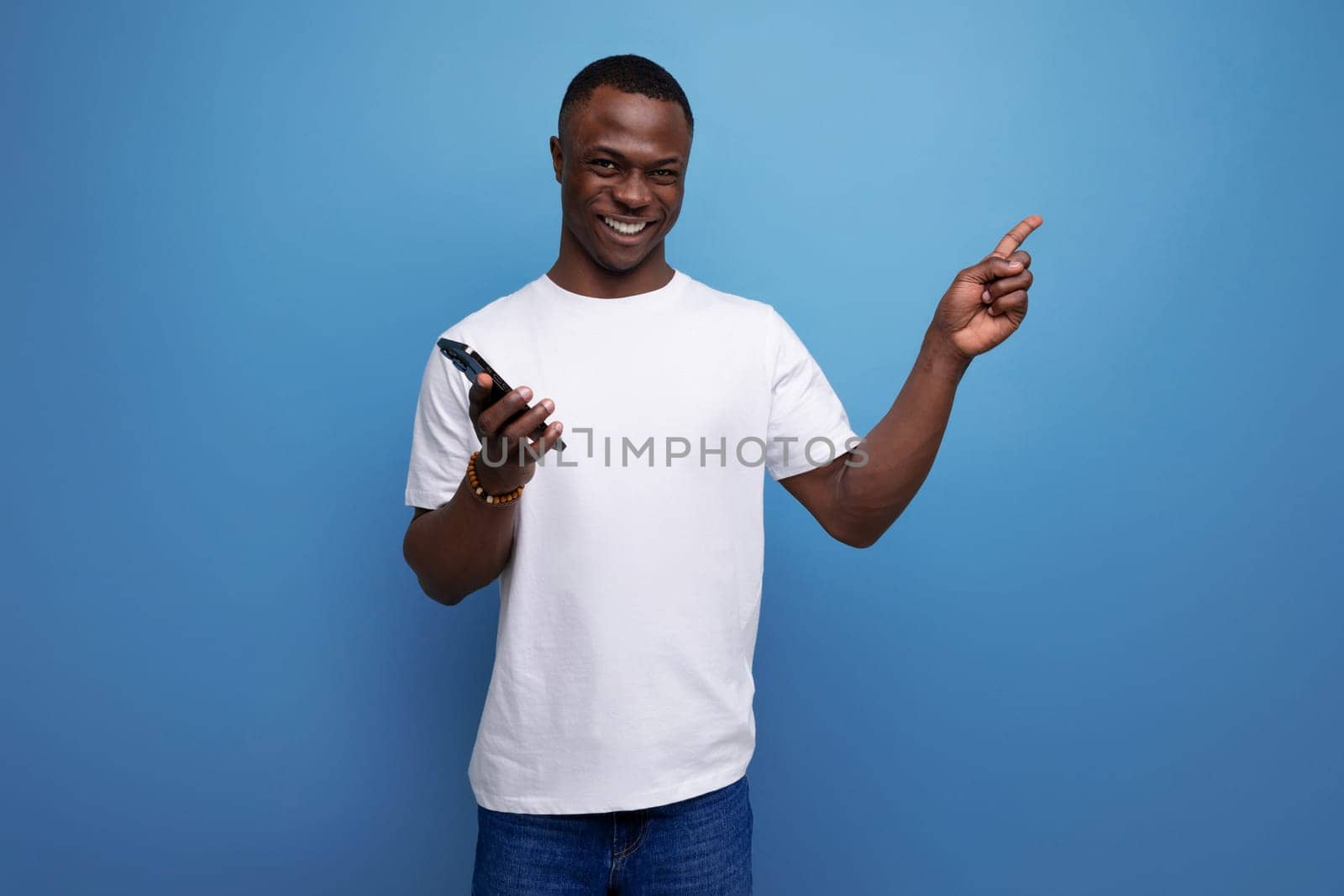 cheerful 30s african man with short haircut in white t-shirt with smartphone.