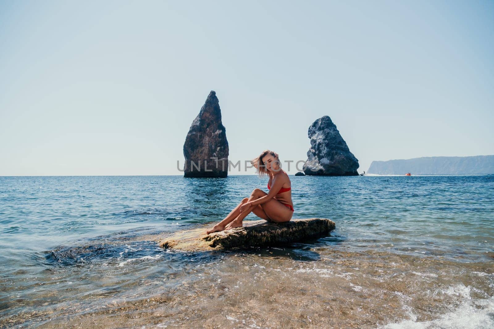 Woman travel sea. Young Happy woman in a long red dress posing on a beach near the sea on background of volcanic rocks, like in Iceland, sharing travel adventure journey