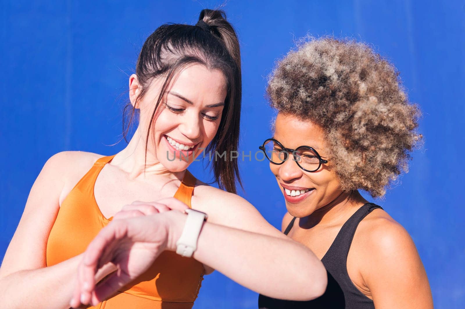 portrait of two multiethnic friends using a smart watch while practicing sport, concept of sports technology and active lifestyle, copy space for text