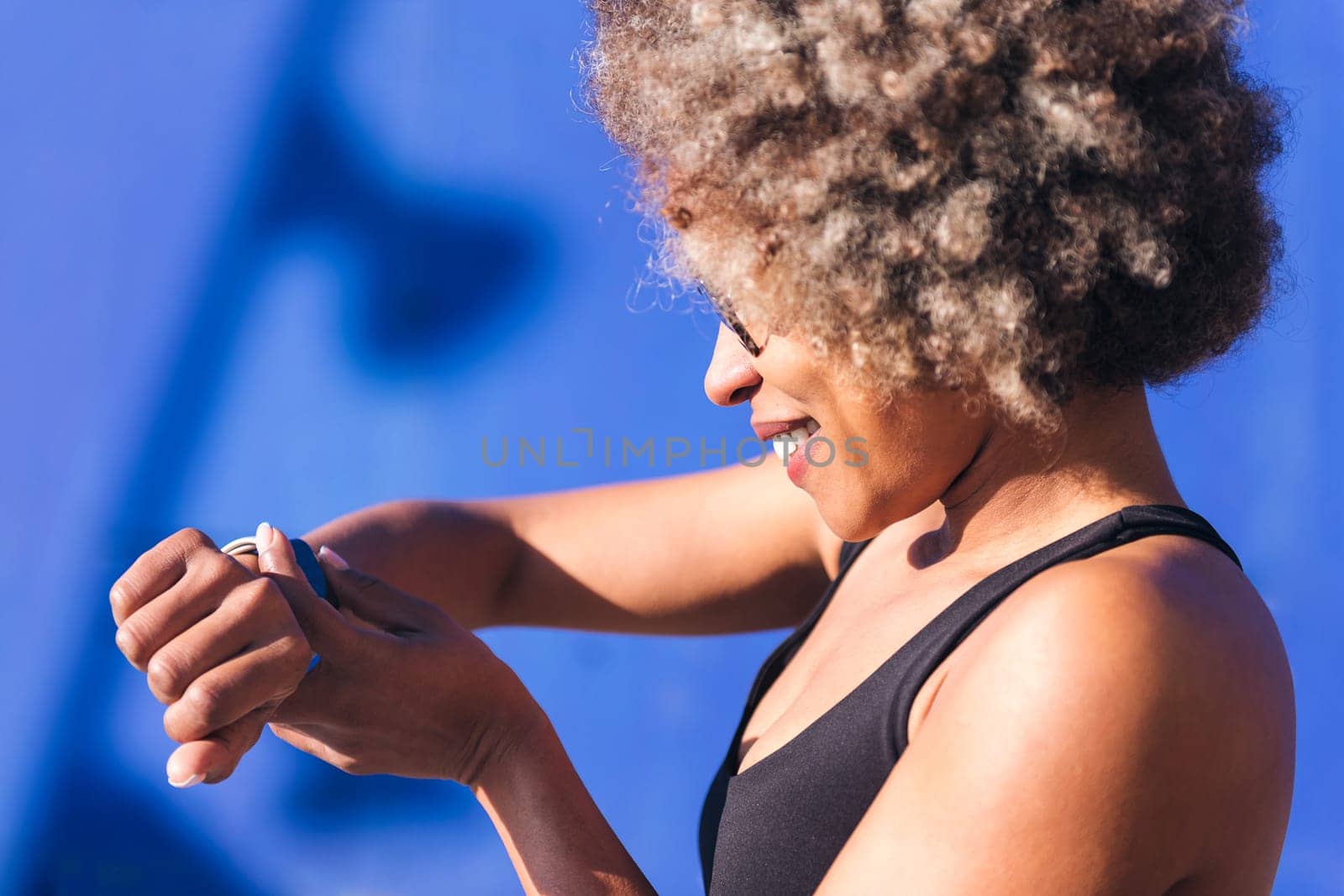 close up profile of a beautiful sportswoman looking at smart watch outdoors in a sunny day, concept of sports technology and active lifestyle, copy space for text