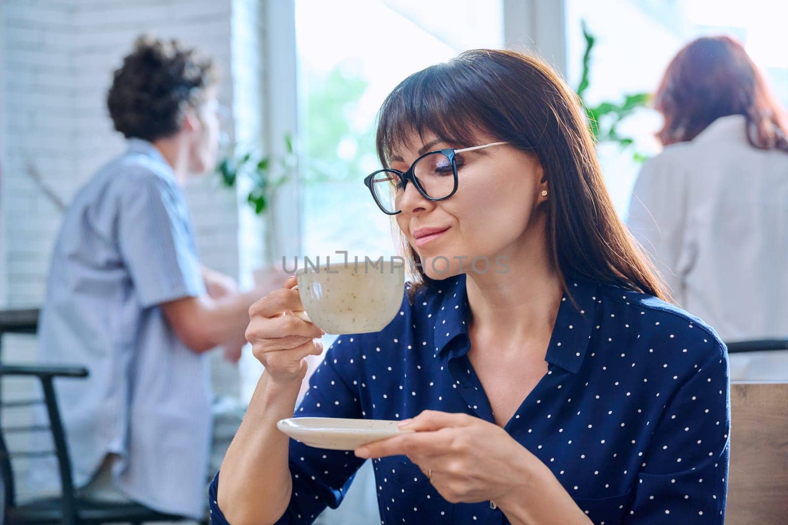 Relaxed middle aged woman enjoying fragrant cup of coffee, in coffee shop by VH-studio
