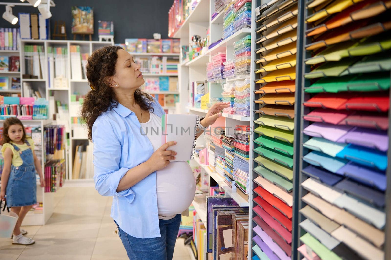 Pregnant woman, inspired painter standing by shelf with color paper sheets, for design, pastel and watercolor painting by artgf