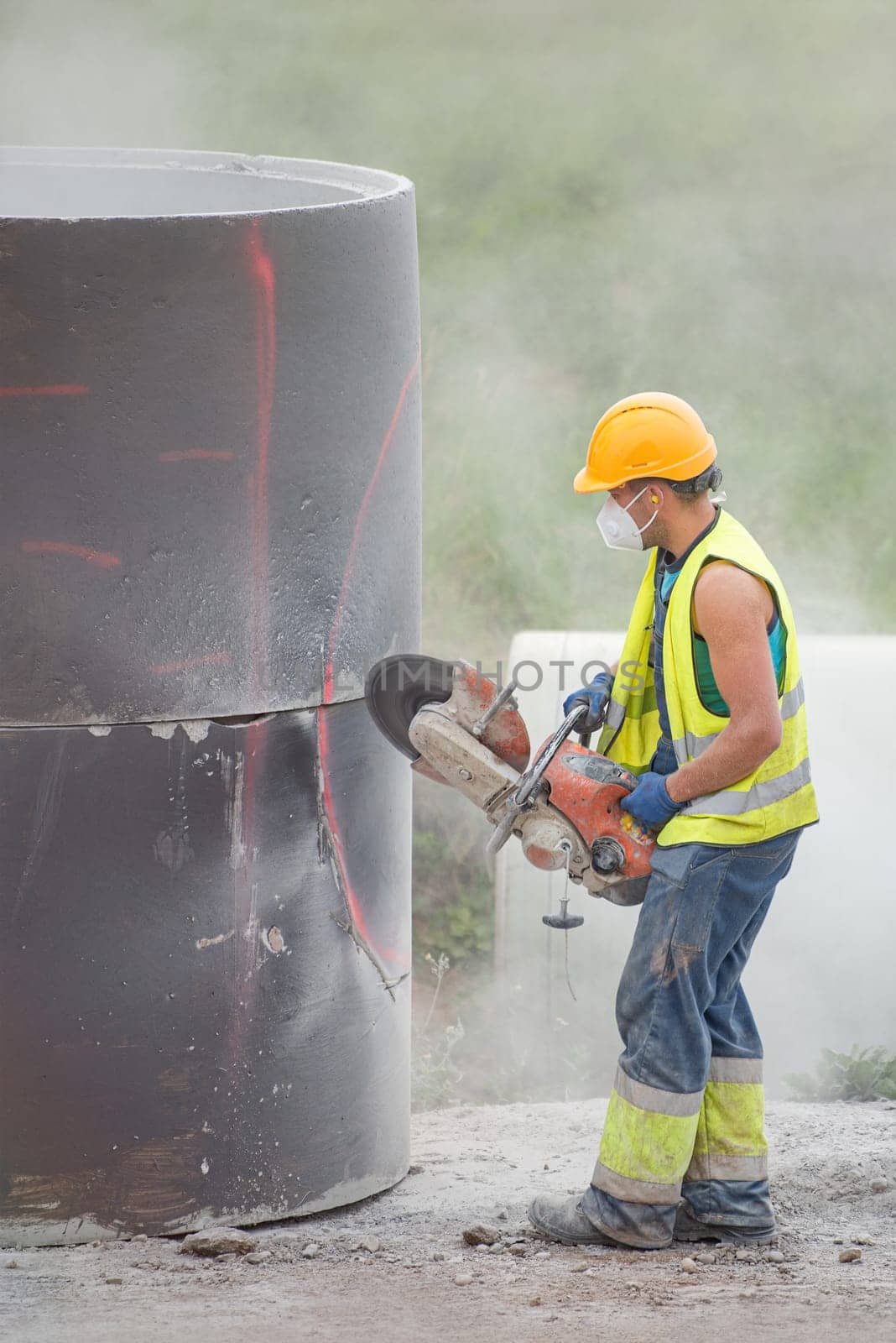 A worker cuts concrete with a special saw. The process of cutting a hole in a concrete ring designed to be buried underground. Dust scatters in different directions during the sawing process. by SERSOL