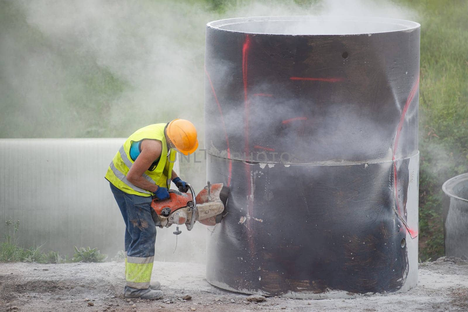 Reconstruction of the road in the city. A worker cuts holes in a concrete barrel to collect rainwater installed under the pavement. Use of a helmet and respirator, compliance with safety regulations. by SERSOL