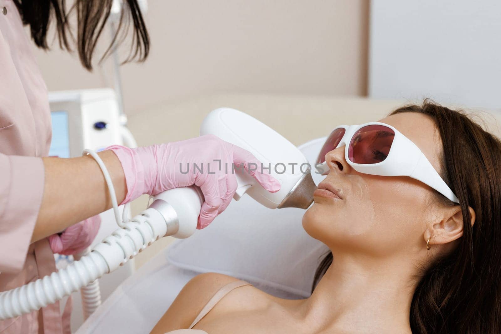 Facial hair removal. Woman patient in glasses receiving a laser hair removal procedure. Apparatus for depilation. Skin care, cosmetic procedures.