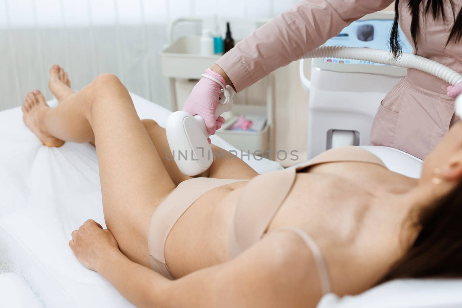 Woman on laser hair removal treatments thighs and bikini area. The procedure of laser hair removal of a young girl abdomen with modern tools by a professional specialist in the clinic. Epilation.