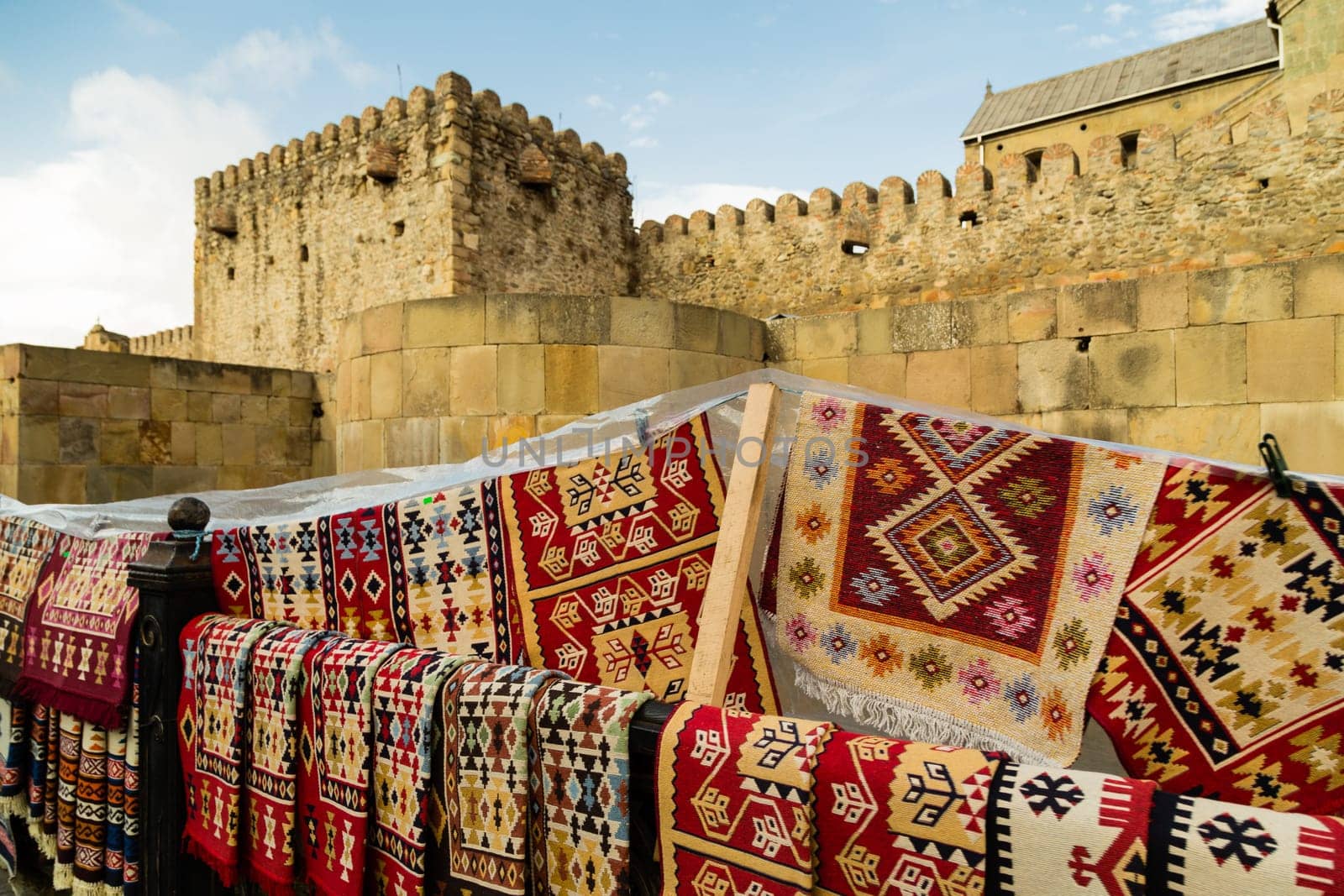 Europe, Georgia - stone yellow wall of an ancient temple, handmade carpets with beautiful ornaments for sale. High quality photo