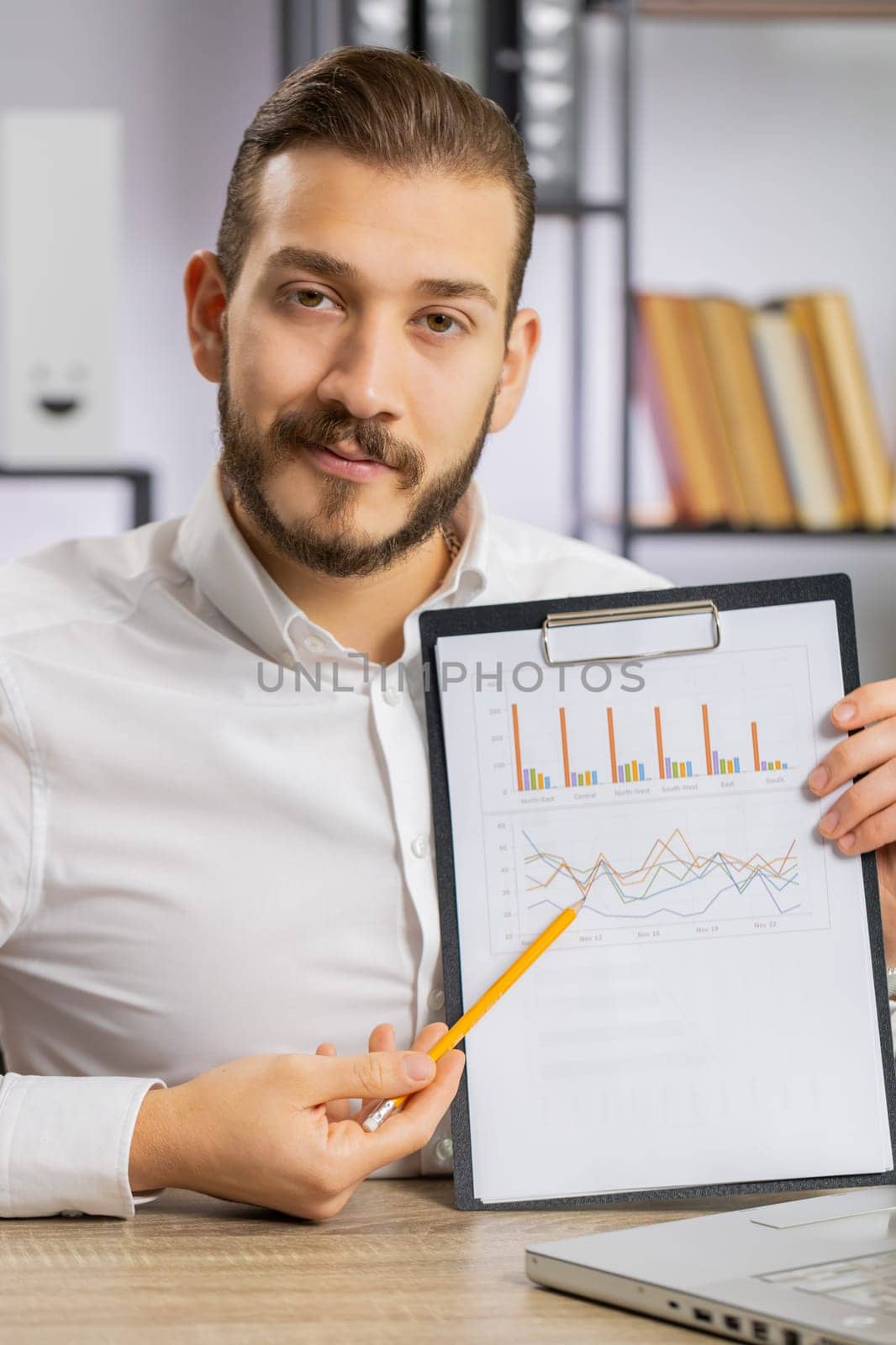 Young boss business man making online presentation video call, demonstrates graphic analytics, planning budget, statistic. Freelancer guy at office workplace looking at camera, talking. Vertical shot