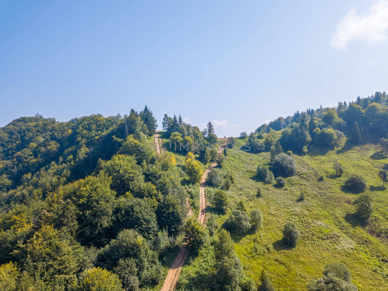 Summer forest road among hills and blue sky. Aerial drone view