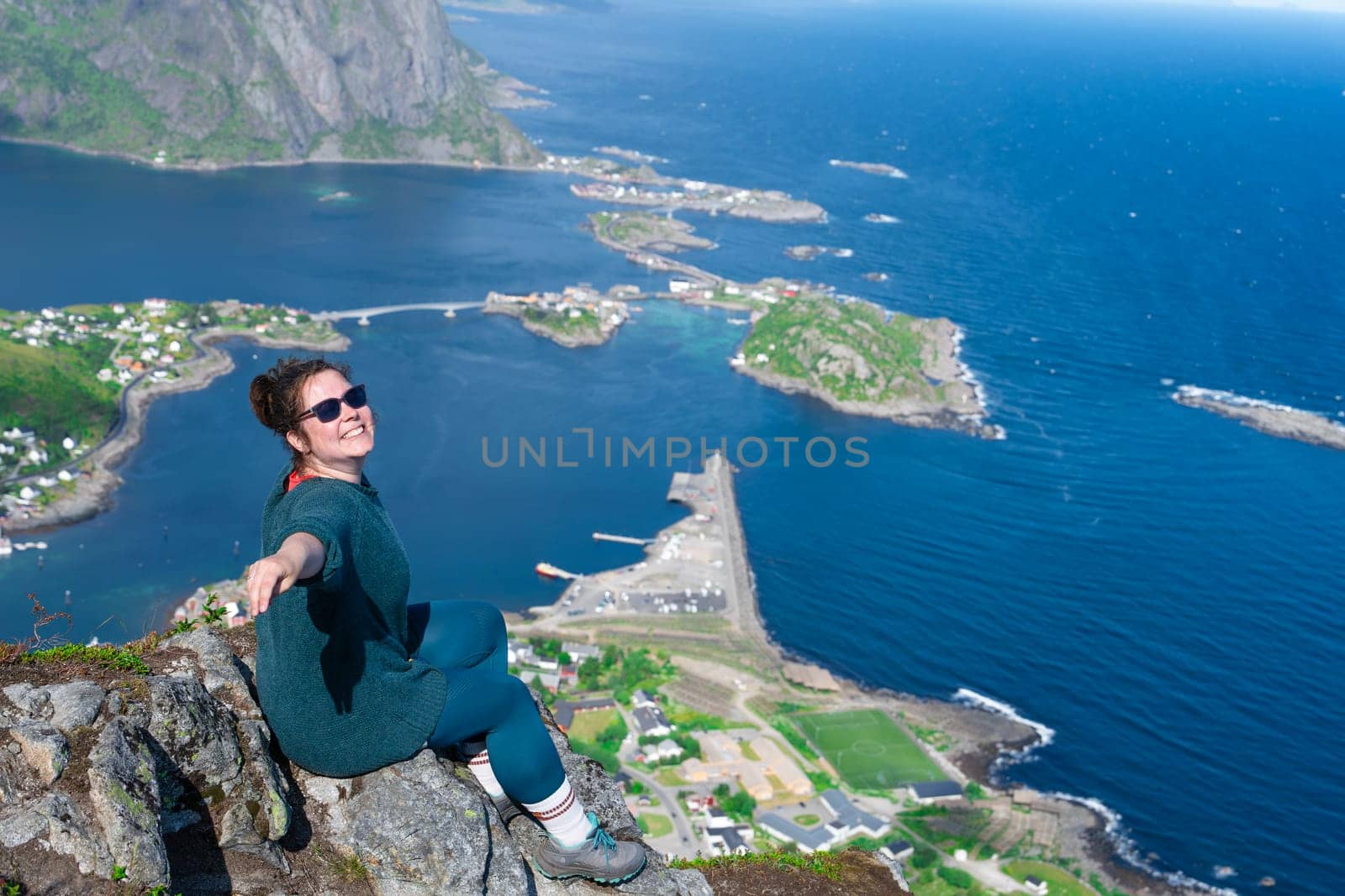 Happy woman hiker enjoys the panorama of lofoten islands at the top of Reinebringen. traveler alone on cliff edge in Norway lifestyle exploring concept. Hike above Reine village in the Lofoten archipelago, travel to Norway