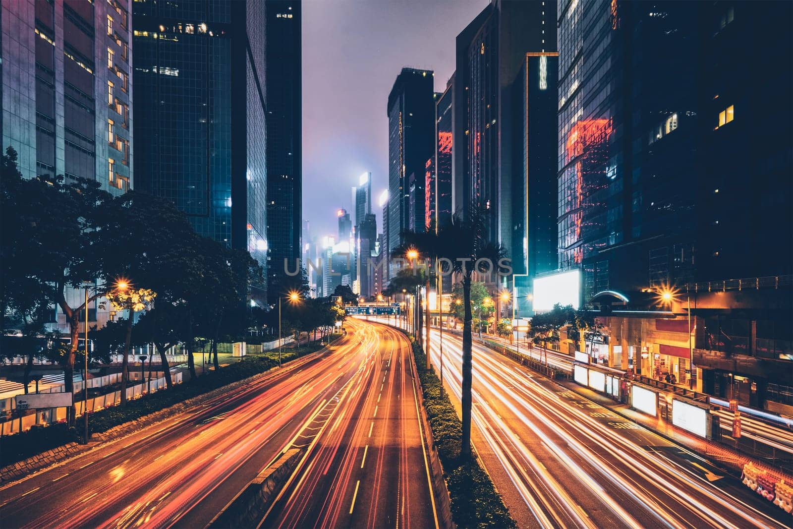 Street traffic in Hong Kong at night. Office skyscraper buildings and busy traffic on highway road with blurred cars light trails. Hong Kong, China