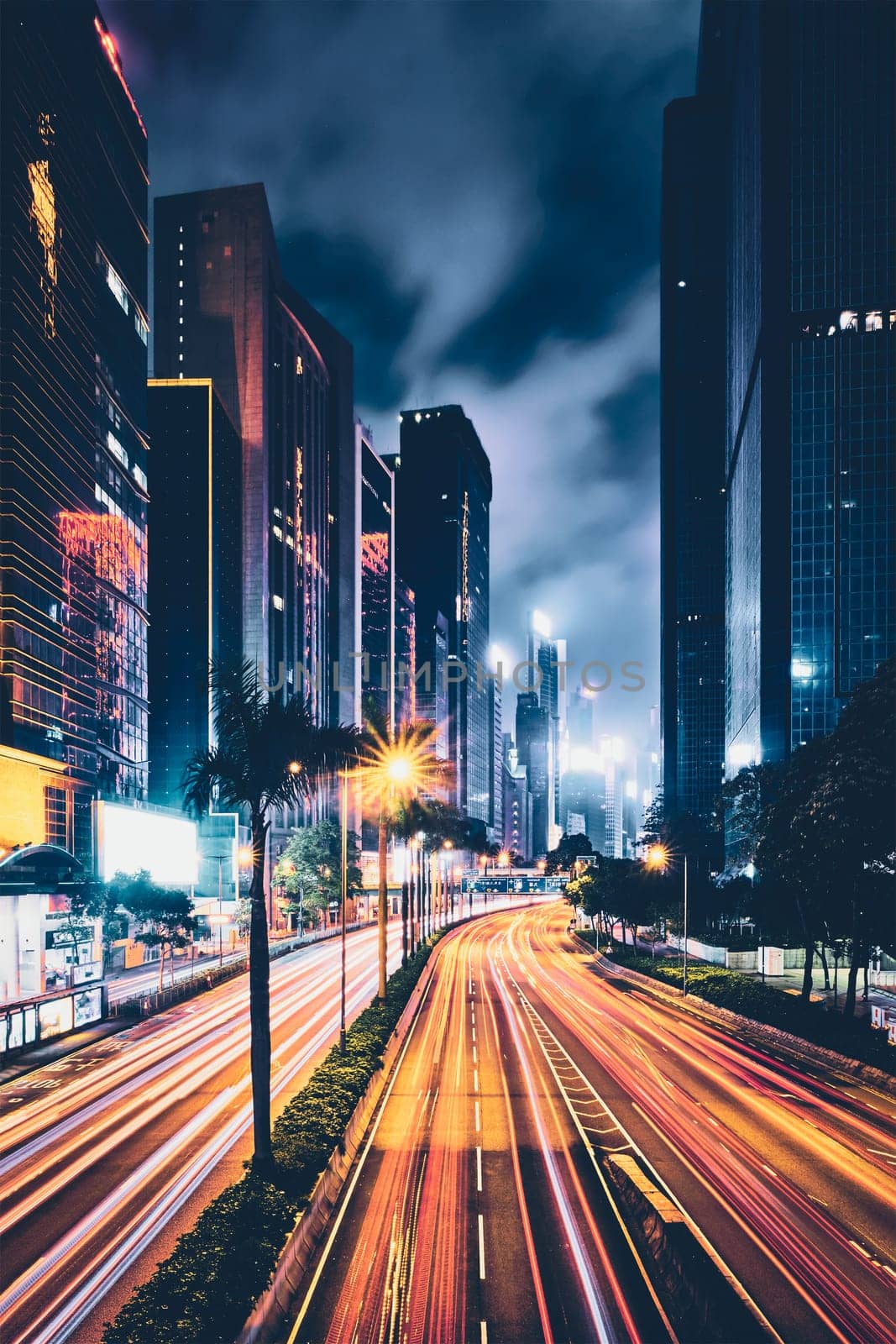 Street traffic in Hong Kong at night. Office skyscraper buildings and busy traffic on highway road with blurred cars light trails. Hong Kong, China