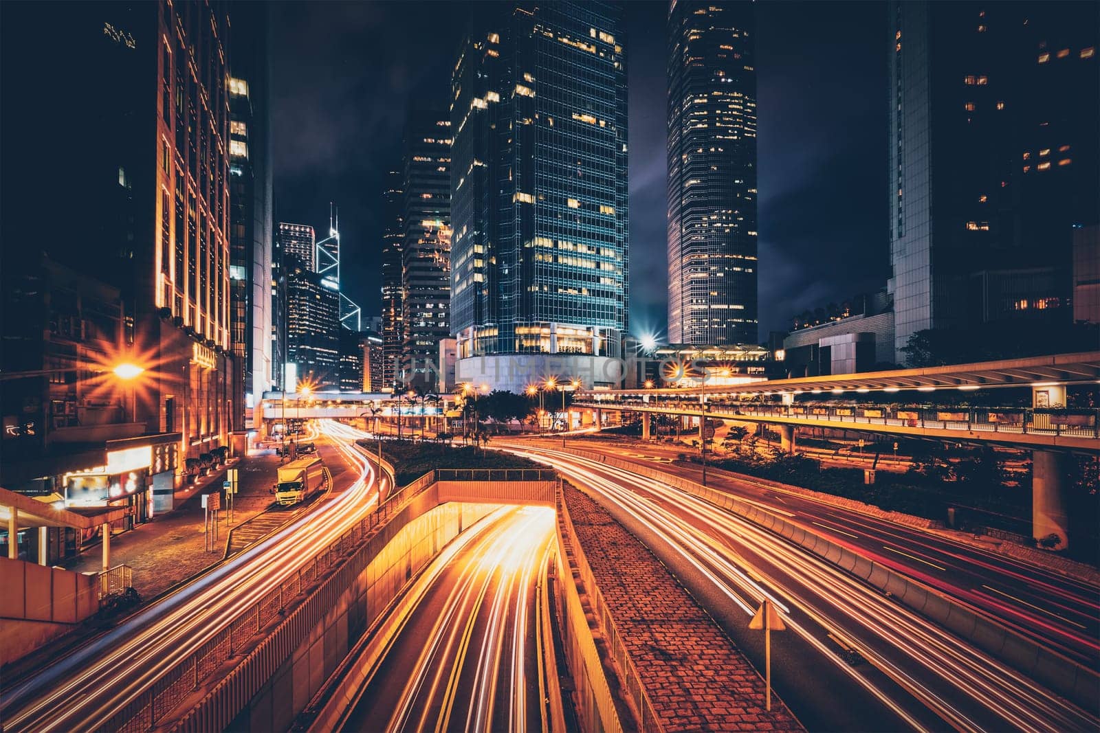 Street traffic in Hong Kong at night. Office skyscraper buildings and busy traffic on highway road with blurred cars light trails. Hong Kong, China