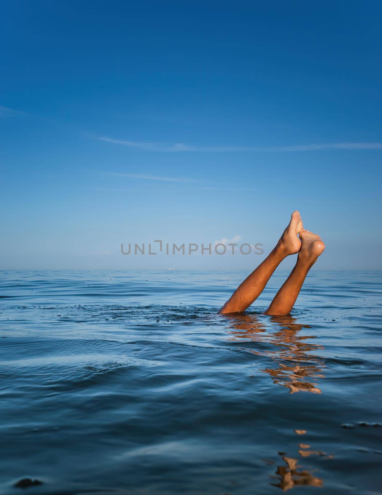 Relaxation and healthy lifestyle. Young boy teenager bathes in the sea. The boy dives and his legs stick out above the water