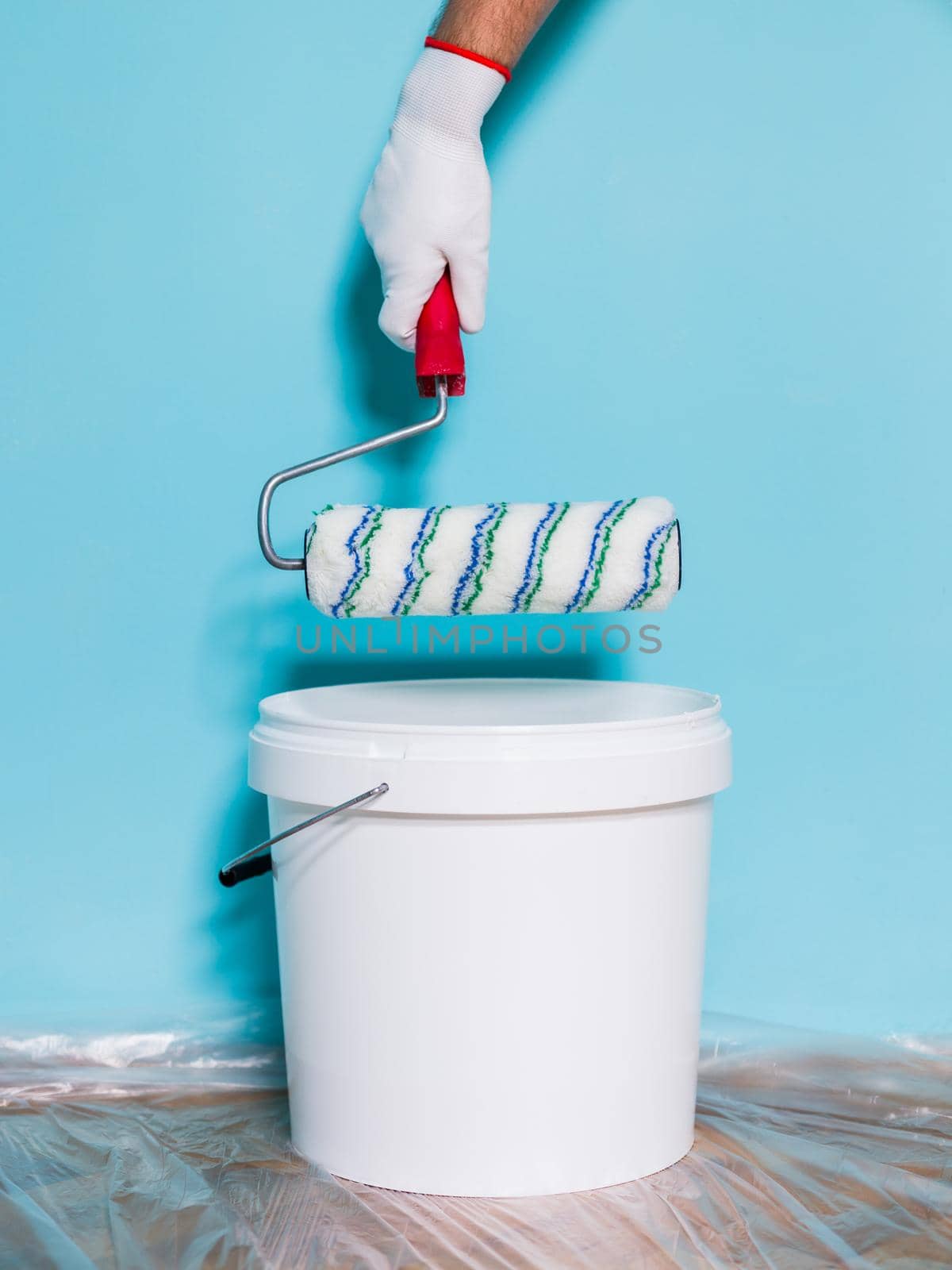 Image of paint can and man holding paint roller in front of blue wall.