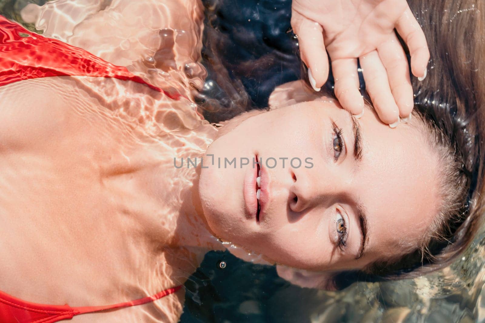 Woman travel portrait. close-up portrait of a happy woman with long hair in a red bikini, floating in water and smiling at the camera. by panophotograph