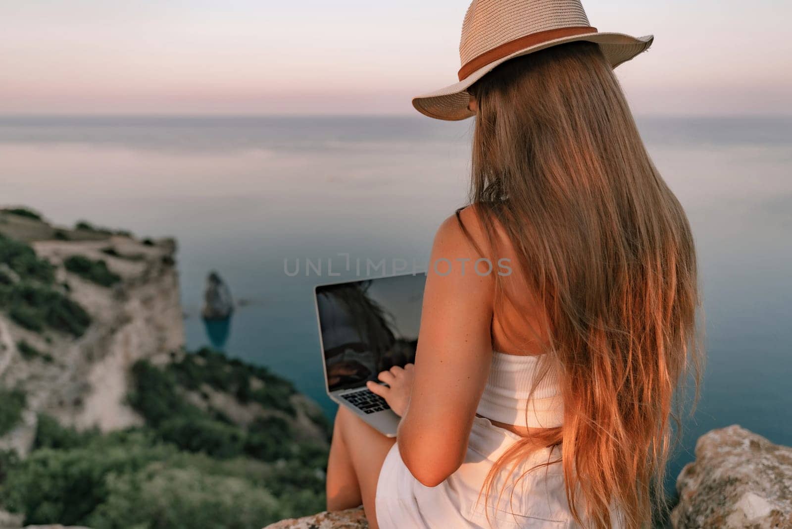 Freelance women sea working on the computer. Good looking middle aged woman typing on a laptop keyboard outdoors with a beautiful sea view. The concept of remote work. by Matiunina