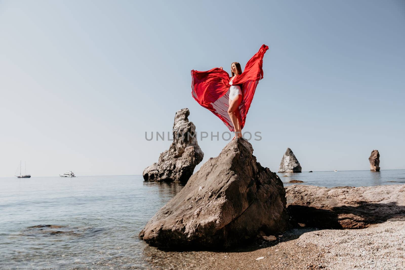 Woman travel sea. Young Happy woman in a long red dress posing on a beach near the sea on background of volcanic rocks, like in Iceland, sharing travel adventure journey by panophotograph