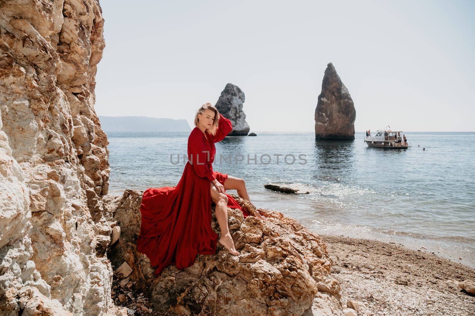 Woman travel sea. Young Happy woman in a long red dress posing on a beach near the sea on background of volcanic rocks, like in Iceland, sharing travel adventure journey