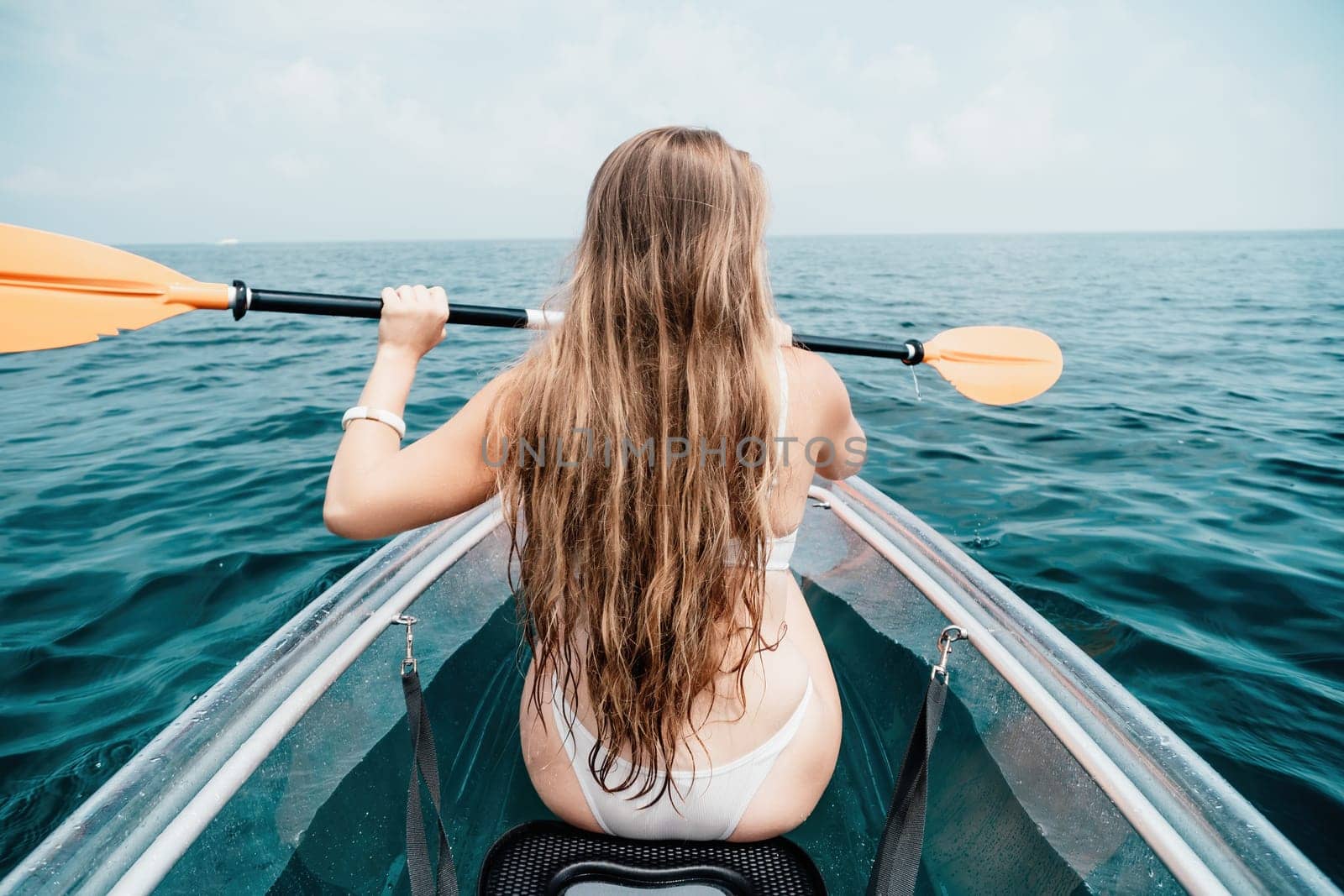 Woman in kayak back view. Happy young woman with long hair floating in transparent kayak on the crystal clear sea. Summer holiday vacation and cheerful female people having fun on the boat.