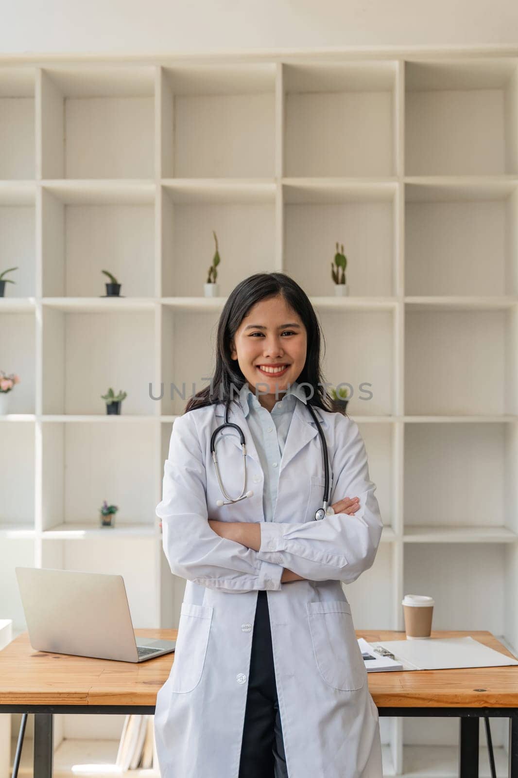 Beautiful young asian doctor standing smiling with crossed arms and stethoscope in office at hospital by nateemee