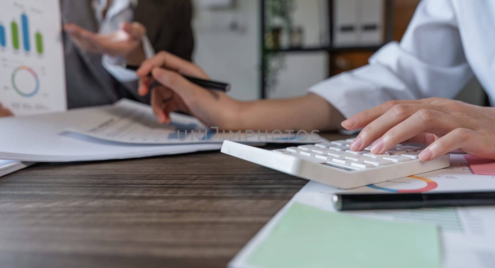 Teamwork of business two colleagues analysis with financial data and marketing report graph, Young business woman two co worker discussing for calculating financial document with calculator.