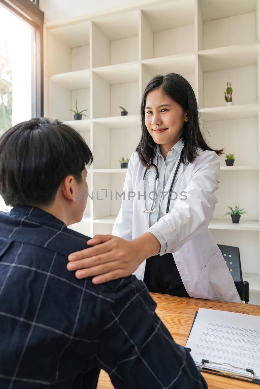Asian female doctor giving hope and encourage to stressed man patient at hospital. Smiling doctor woman touching on patient shoulder to support take care and helping . Supported and Encouraged by nateemee