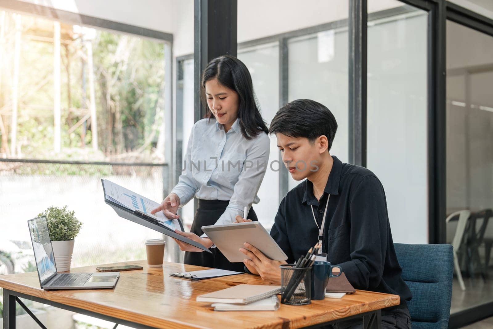 Two Asian businessmen met in the office and pointed to analysis charts and graphs of business growth and financial performance.