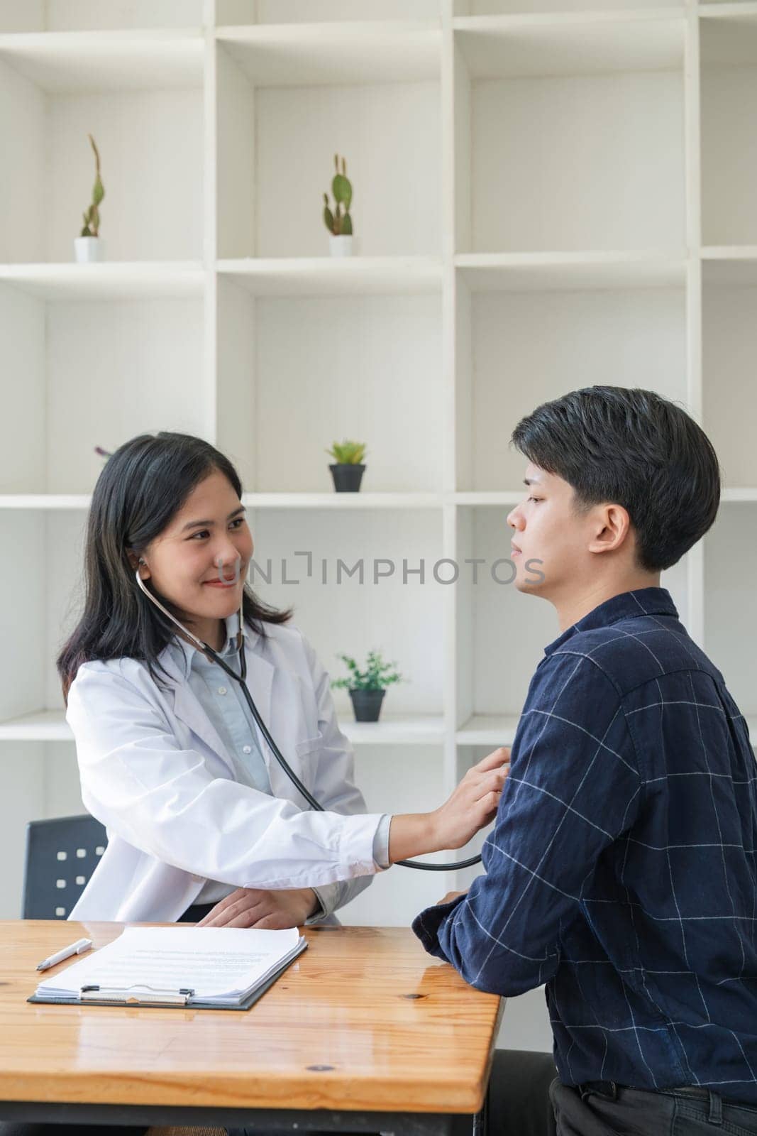 Asian man patient are checked up his health while a woman doctor use a stethoscope to hear heart rate of him.