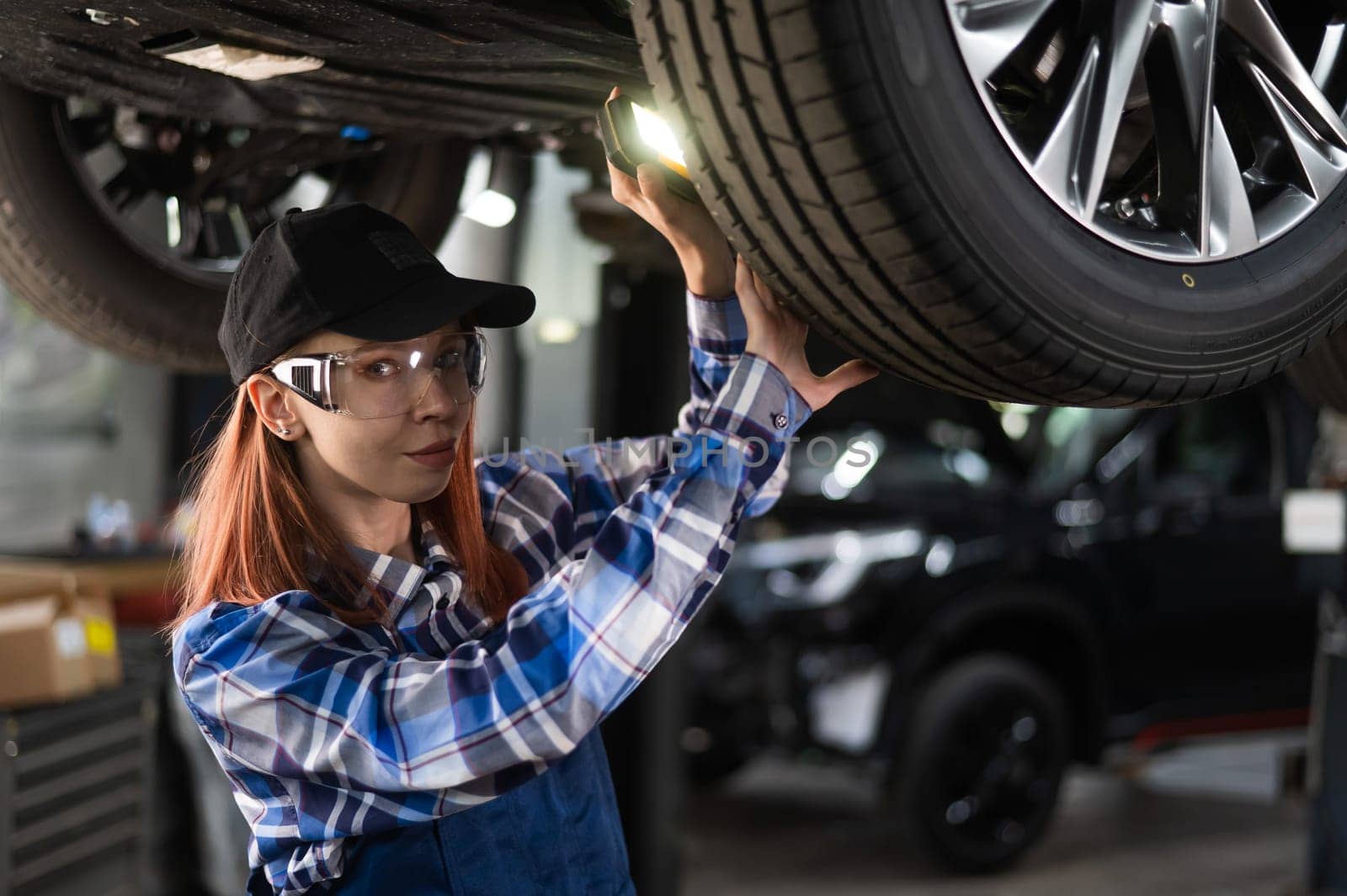 A female mechanic inspects a lifted car. A girl at a man's work. by mrwed54