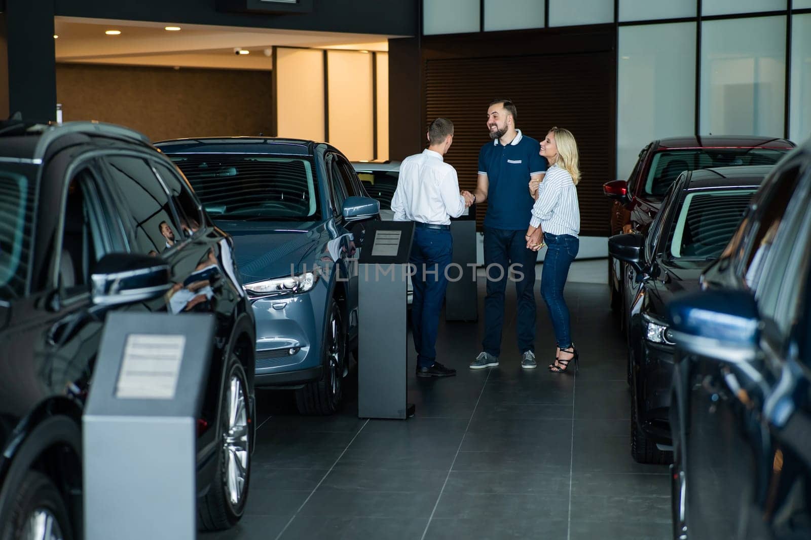A caucasian couple shakes hands with a salesperson while buying a car. by mrwed54