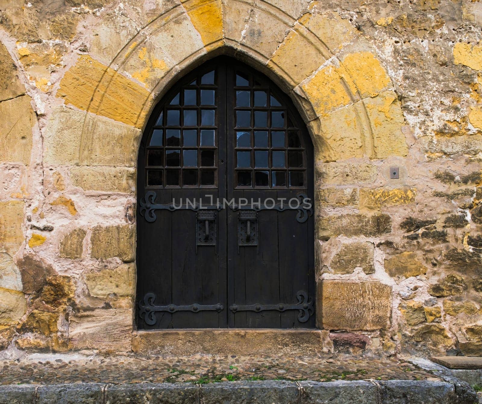 Ancient dark wooden door with pointed arch in stone wall. by csbphoto