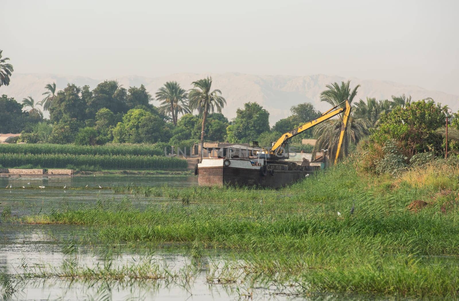 Panoramic landscape view across african river with large dredging barge boat working on river bank