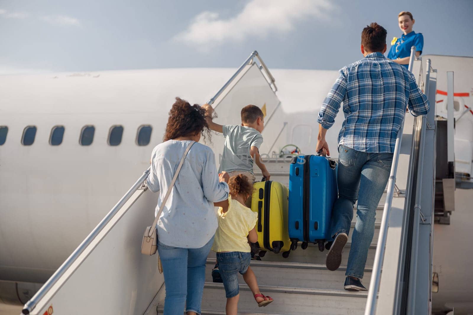 Back view of family of four getting on, boarding the plane on a daytime, ready for summer vacations. People, traveling, vacation concept