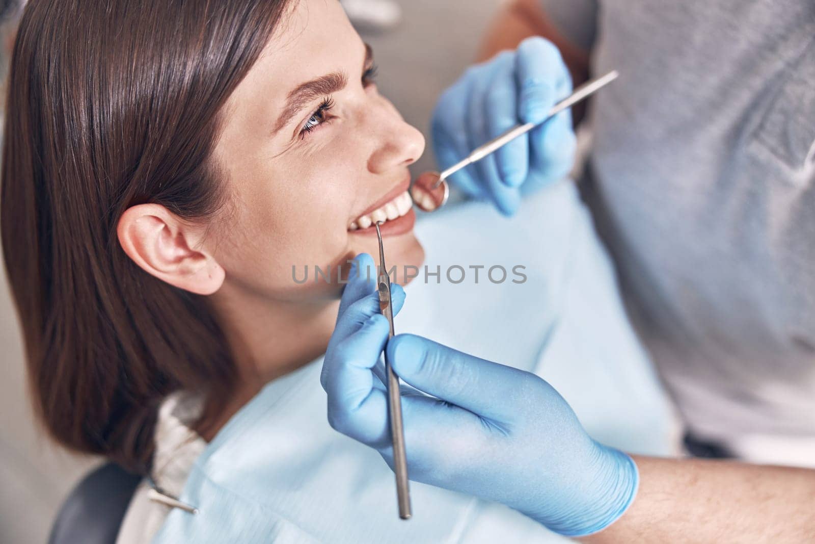 Confident mature doctor is checking teeth of young beautiful happy caucasian woman in modern clinic by Yaroslav_astakhov