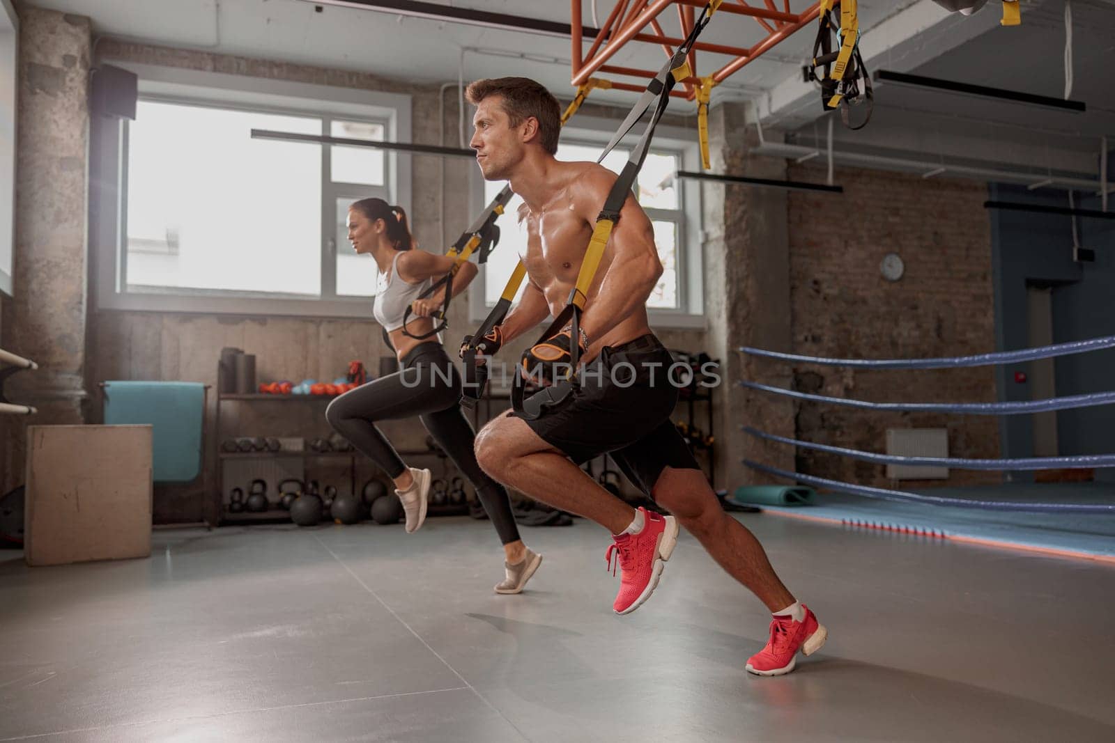 Strong man in training gloves with slender female doing stretching exercises in the gym and looking ahead