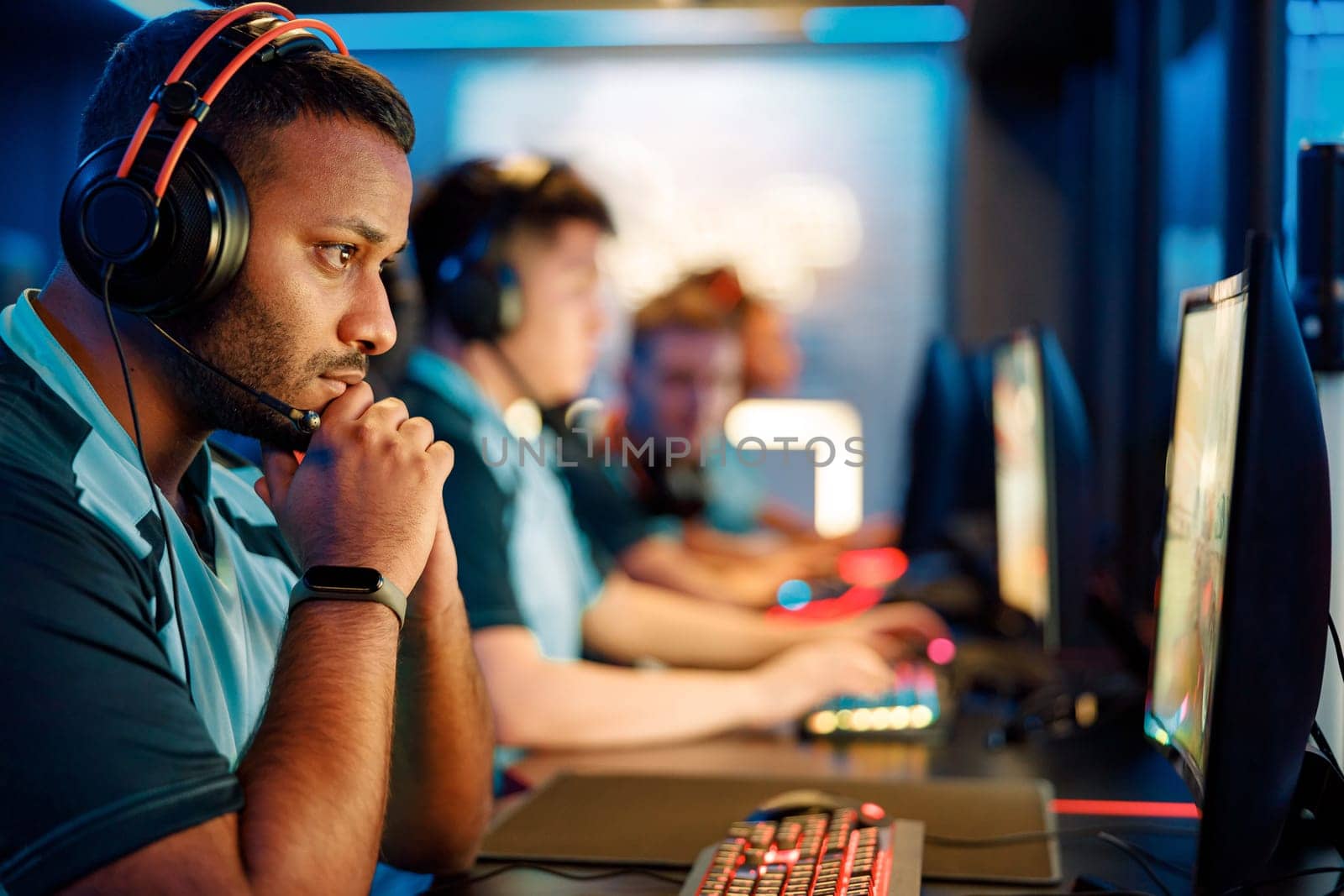Side view of focused African professional gamer wearing headphones looking at PC screen while sitting in gaming club
