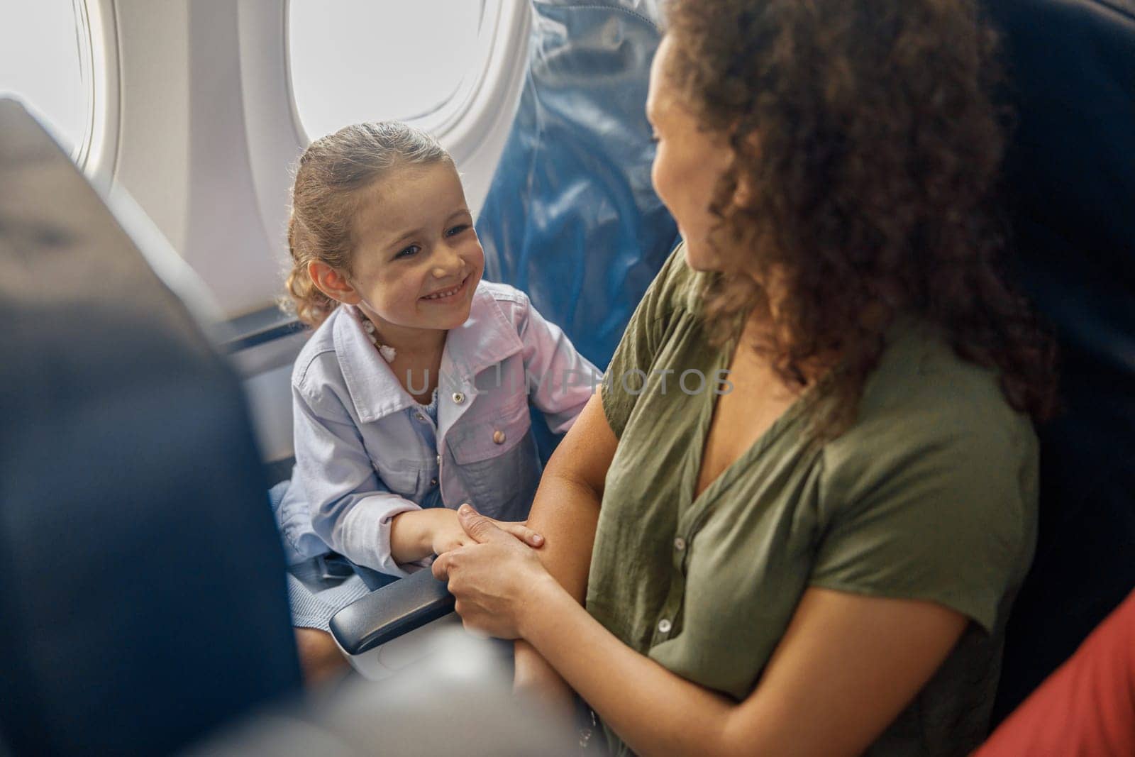 High angle view of little girl sitting on the plane, smiling to her mother while they are traveling together. Family, vacation concept