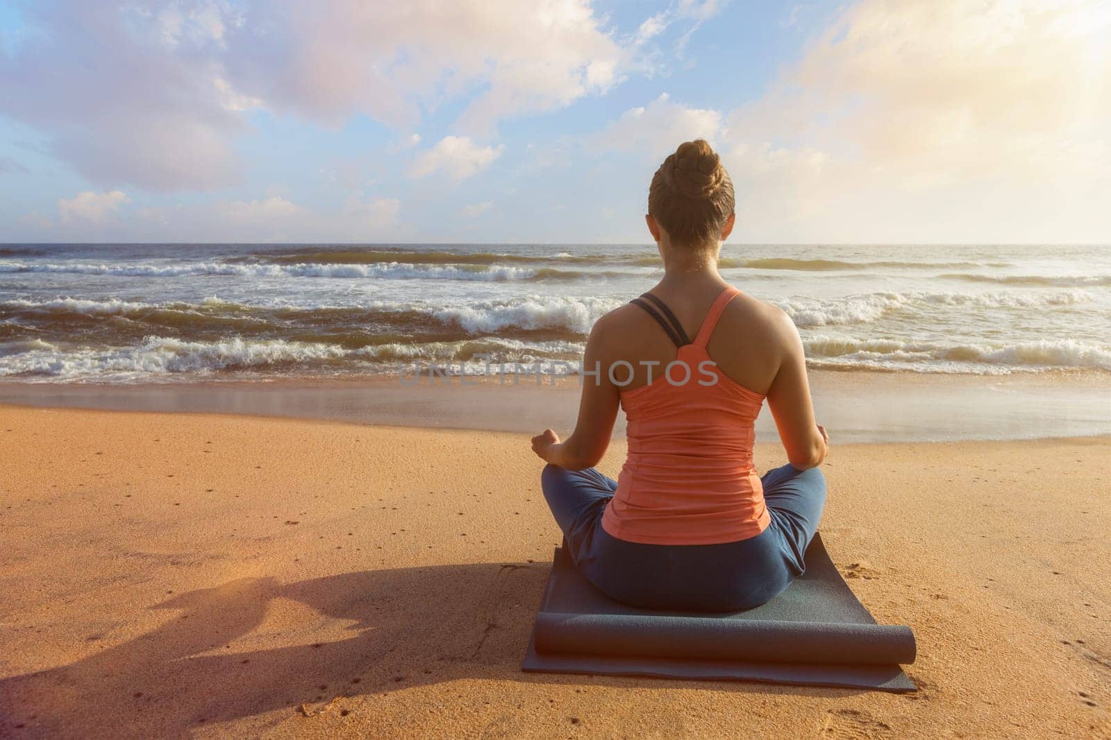 Woman doing yoga oudoors at beach - Padmasana lotus pose by dimol