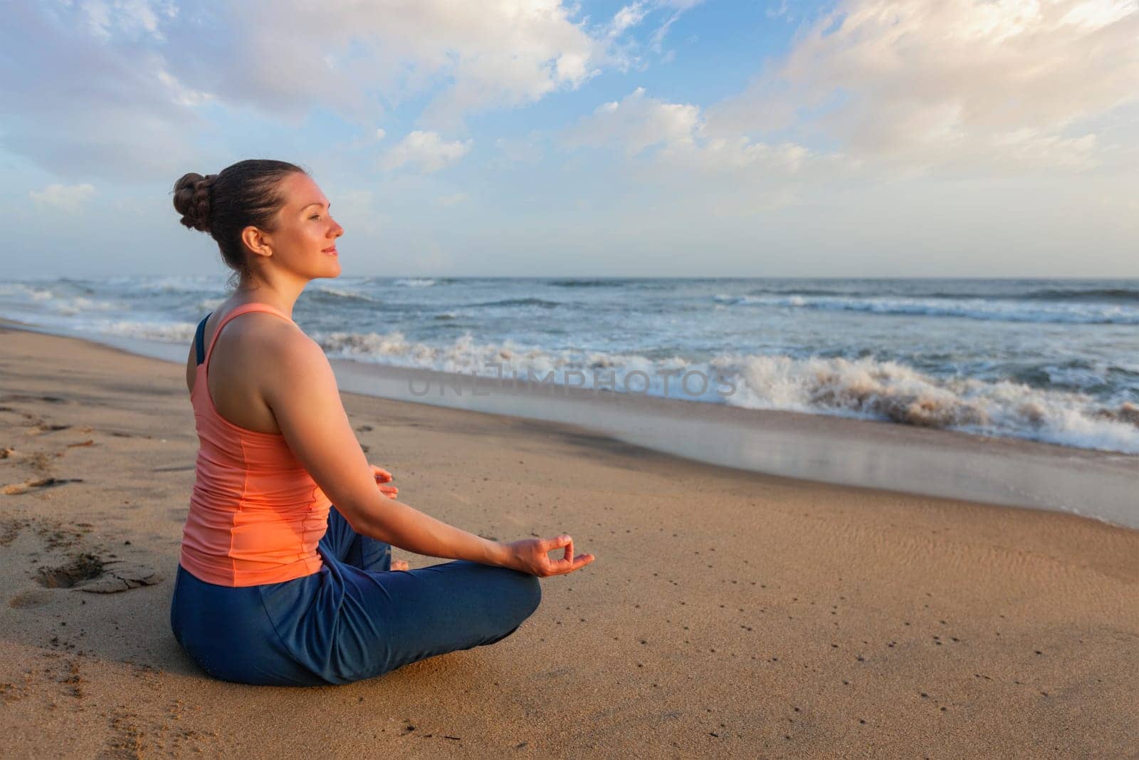 Woman doing yoga - meditate and relax in Padmasana Lotus asana pose with chin mudra outdoors at tropical beach on sunset