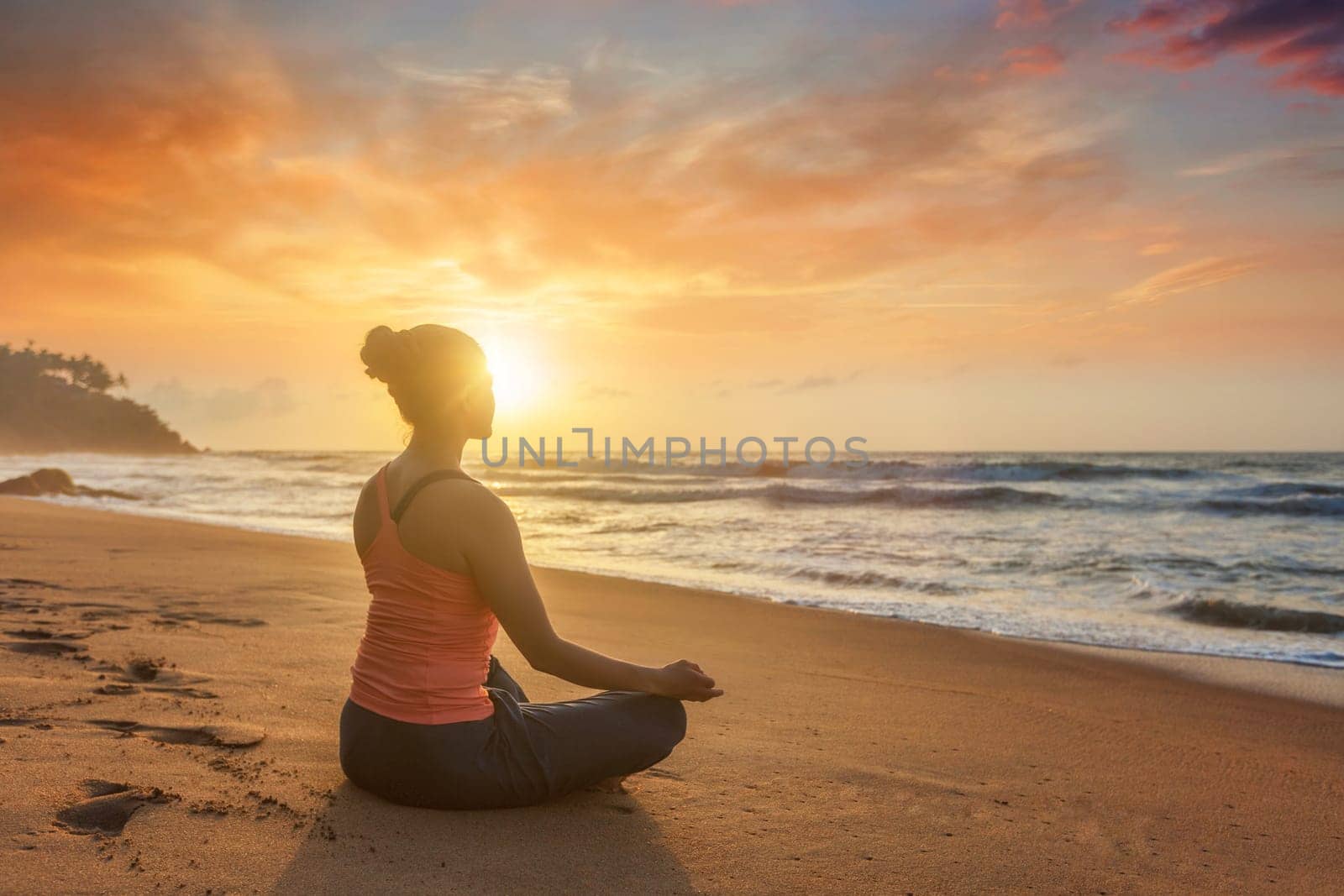 Woman doing yoga - meditate and relax in Padmasana Lotus asana pose with chin mudra outdoors at tropical beach on sunset with dramatic sun